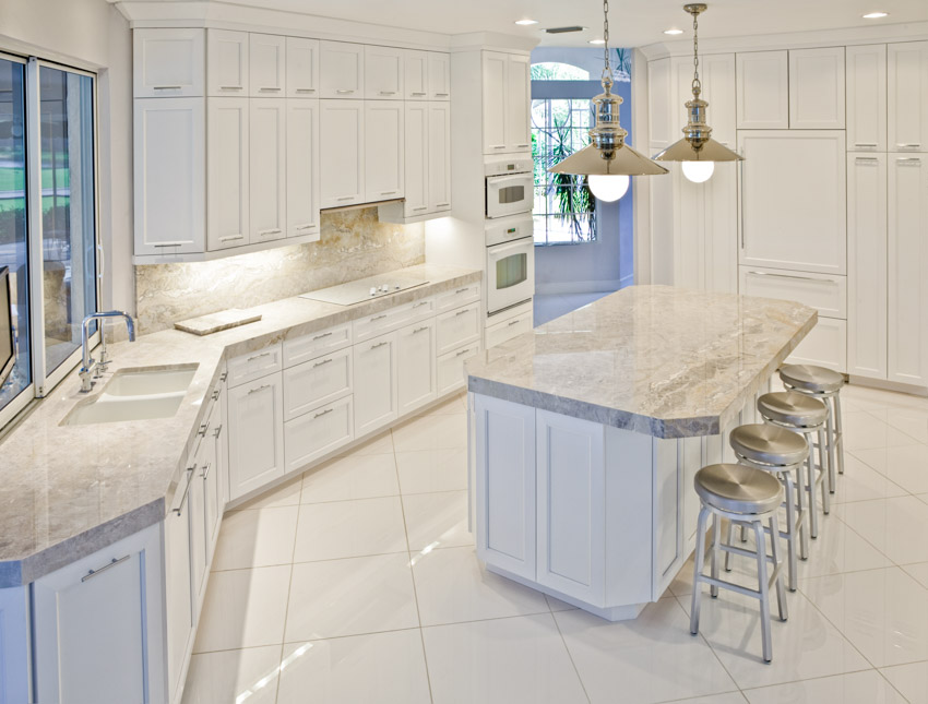 Kitchen with white melamine cabinets, countertops, island, bar stools, hanging lights, tile floors, sink, and faucet