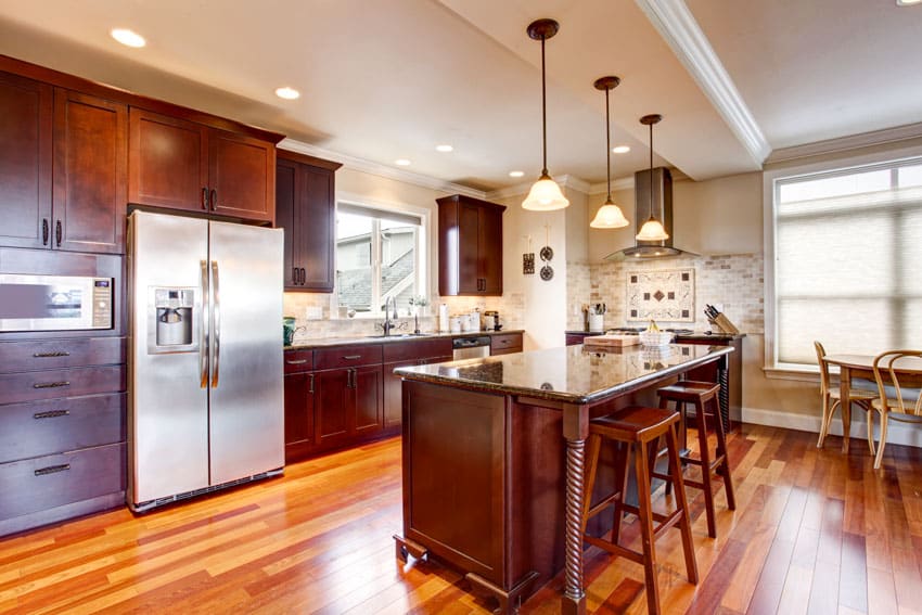 Kitchen with wood floors, island, bar stools, pendant lights, backsplash, refrigerator, and windows