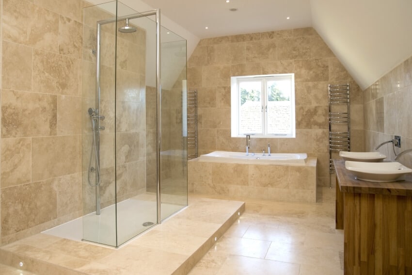 Large bathroom with glass enclosed shower, travertine floors, and double sink on wooden countertop
