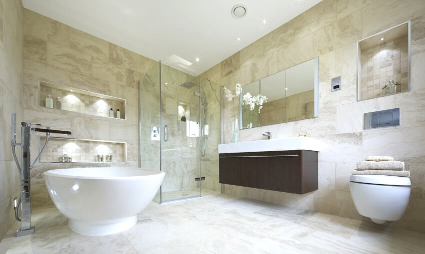 Large bathroom with recessed wall shelves, freestanding tub, and travertine floors