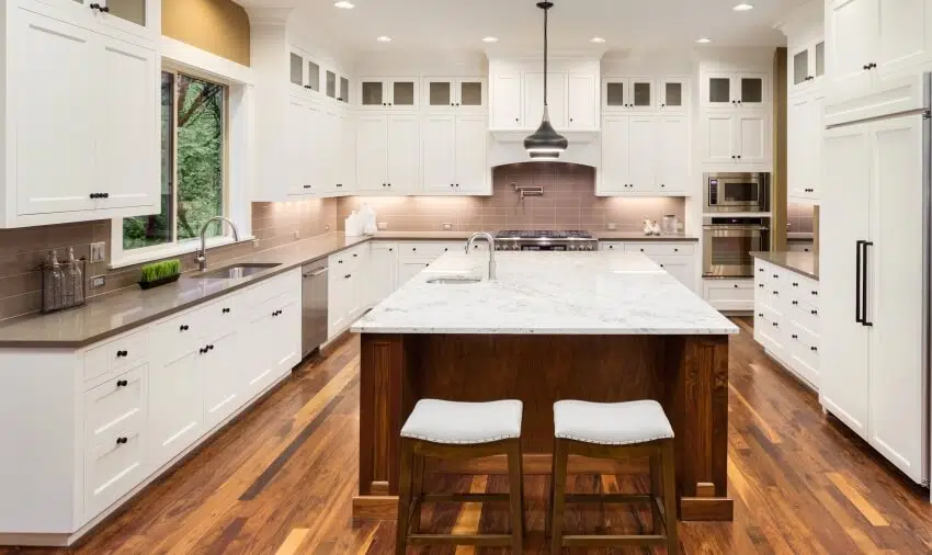 Large kitchen with marbled top island, hardwood floors, and white cabinets with black pulls