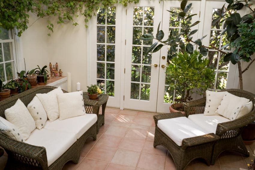 Living room with unglazed terracotta tile floor, cushioned sofa, chair, indoor plants, and glass door