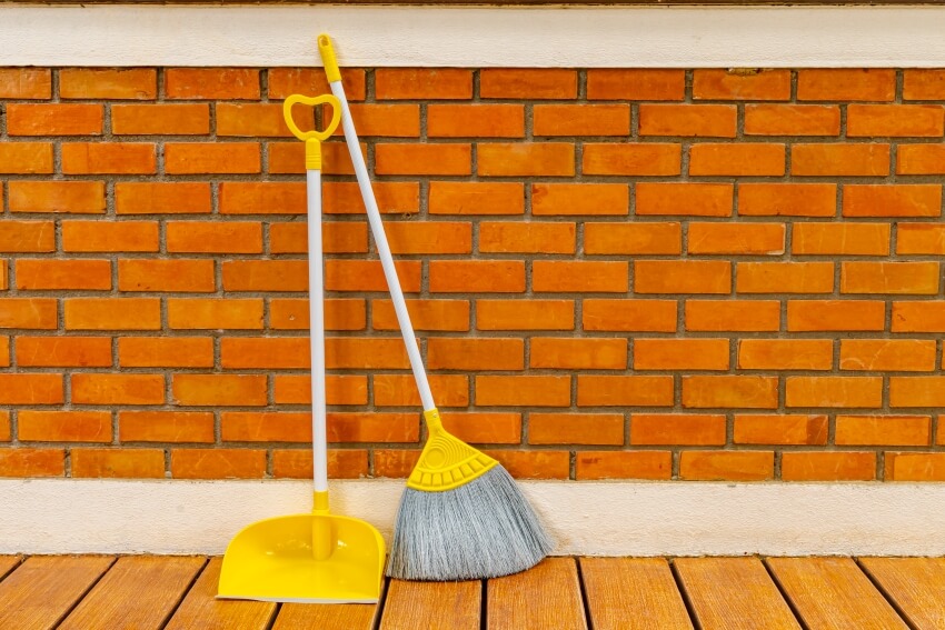 Long handle plastic yellow expandable broom and dustpan prop against a red brick wall 