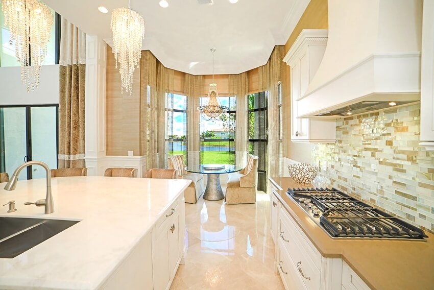 Luxurious kitchen with glass tile backsplash, chandeliers, large island and a sitting area in the corner