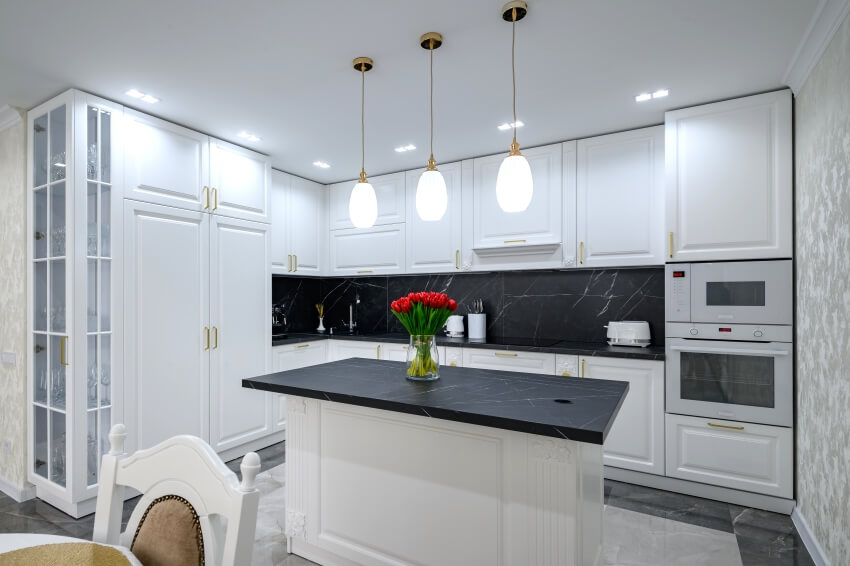 All-white kitchen with center island, lights and black marble backsplash