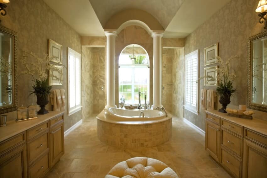 Luxury bathroom with spa tub by the arched window, columns, and travertine floor