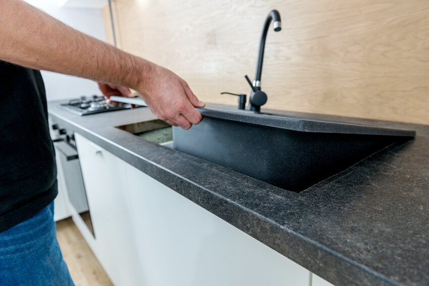 Man installing a dark drop in sink in the kitchen