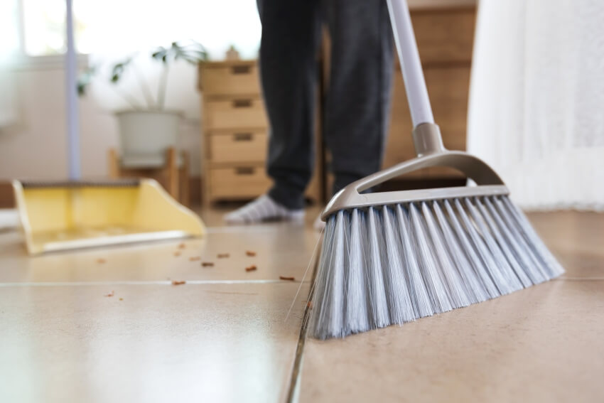 A man sweeping wooden floor with synthetic fibers broom at home