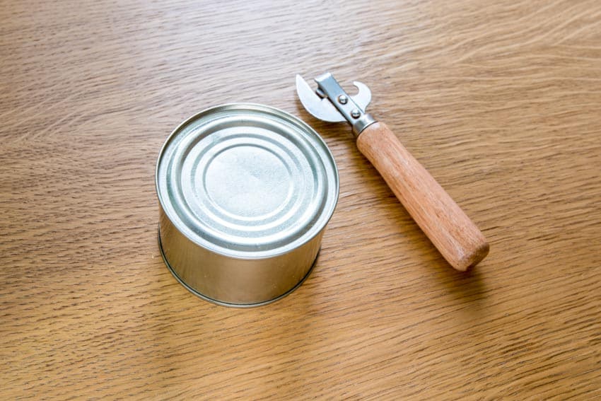 Manual can opener and can on wood kitchen surface