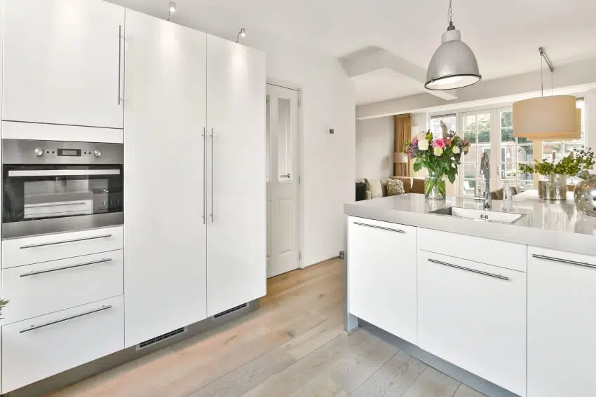 Minimalist kitchen with hardwood floors, and white cabinets with extra long pulls