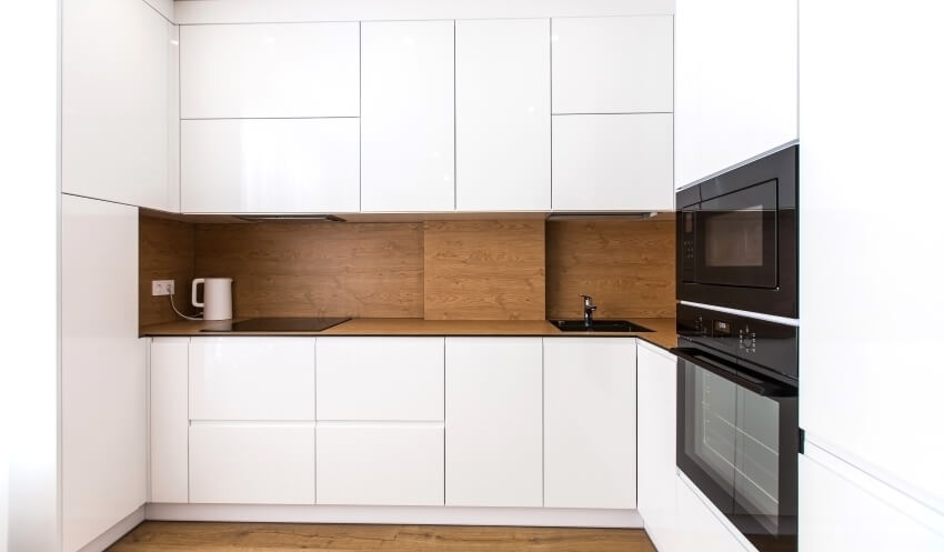 Minimalist white kitchen with wooden backsplash, black appliances, and hardwood floors