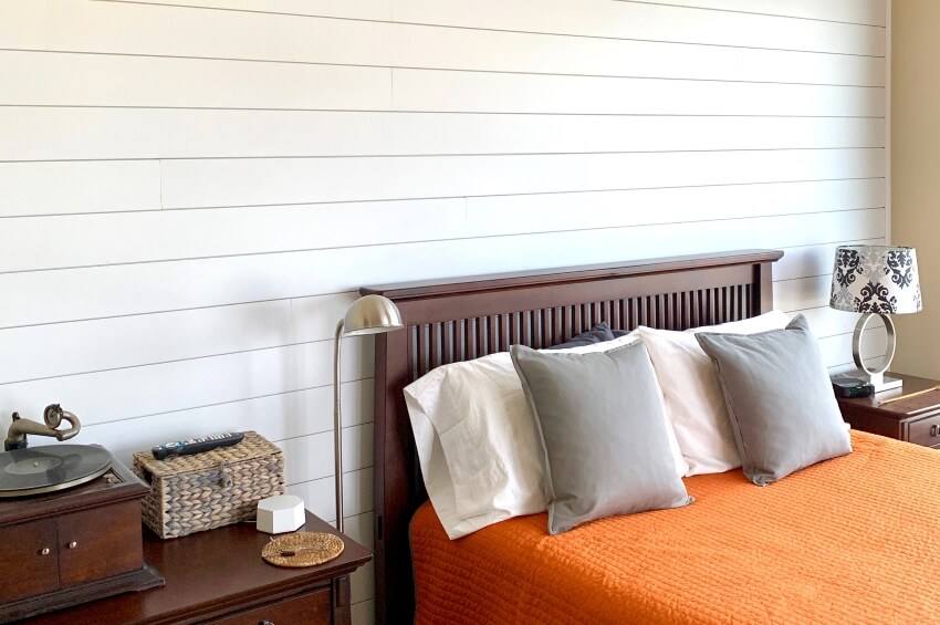 Nickel gap shiplap panel accent wall in bedroom with dark wood furniture and an orange bedspread