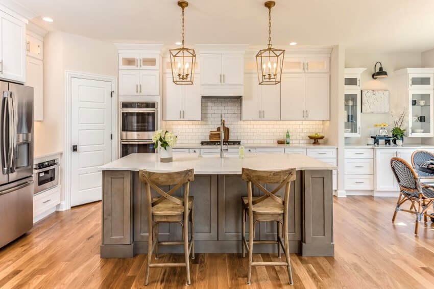 Open kitchen with hardwood floors, pendant lights over island, and white cabinets with silver pulls