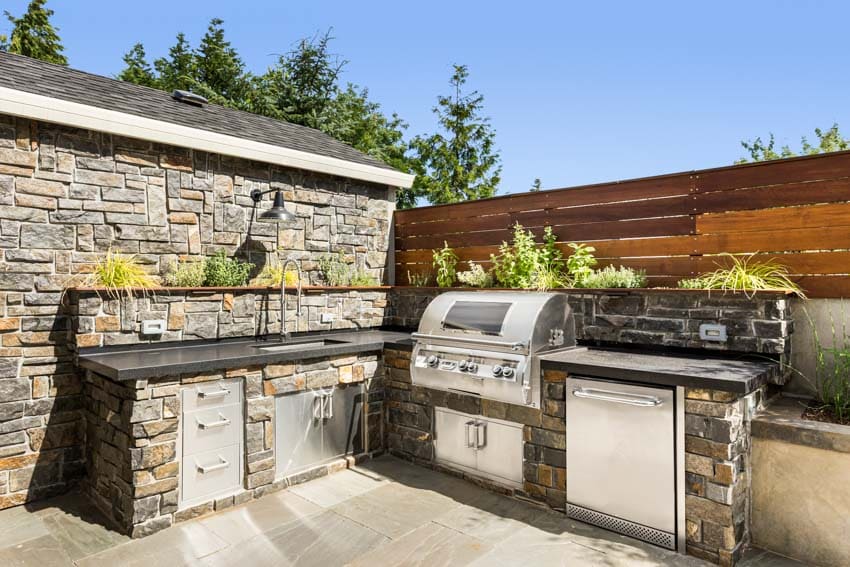Kitchen with stone backsplash, countertop, grill, and wood fence