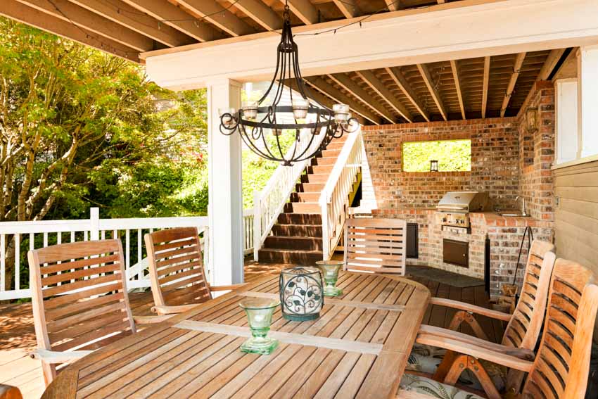 Outdoor kitchen with brick backsplash, grill table, chairs, chandelier, and wood beam ceiling