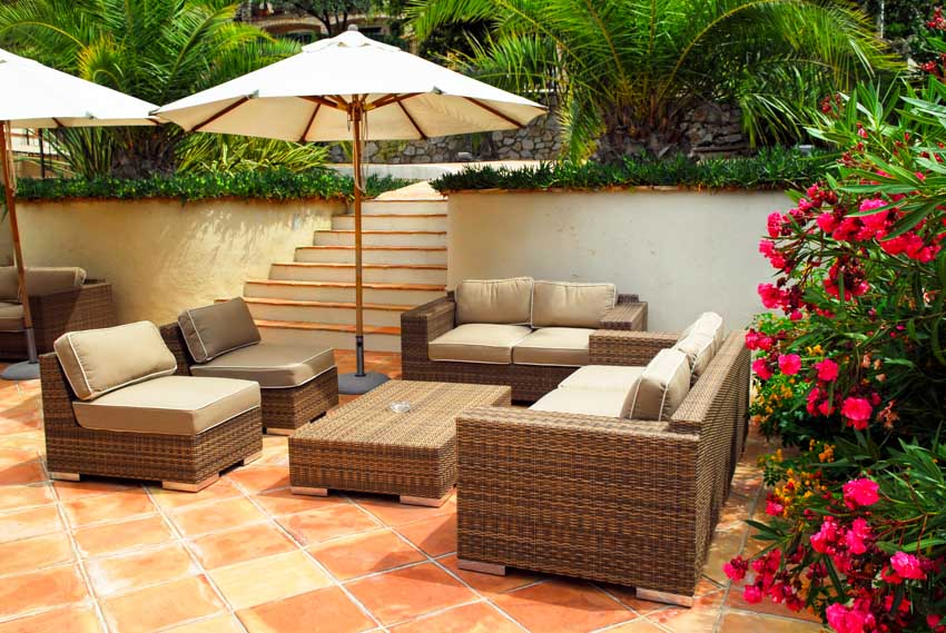 Outdoor patio with Saltillo tile floors, wicker sofa, chairs, coffee table, flowers, and umbrella shade