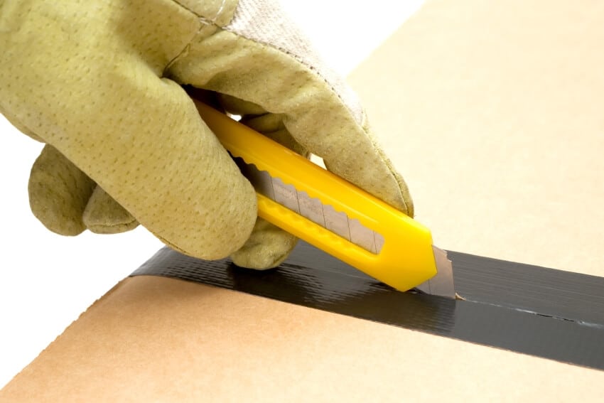 Person in work gloves using a utility knife to open a sealed cardboard box