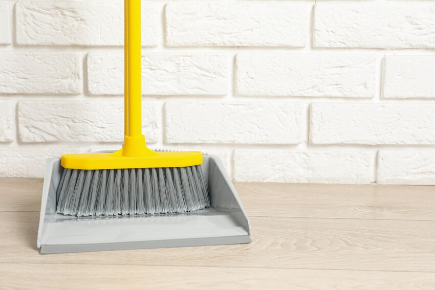 A plastic standard broom with dustpan near white brick wall