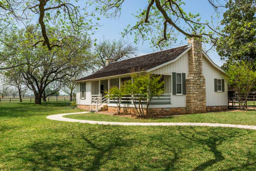 Ranch house with pitched roof, chimney, front porch, patio, windows, and lawn