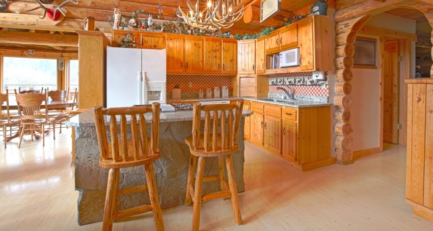 Red cedar cabinets and stone island with wooden chairs in a rustic log cabin kitchen
