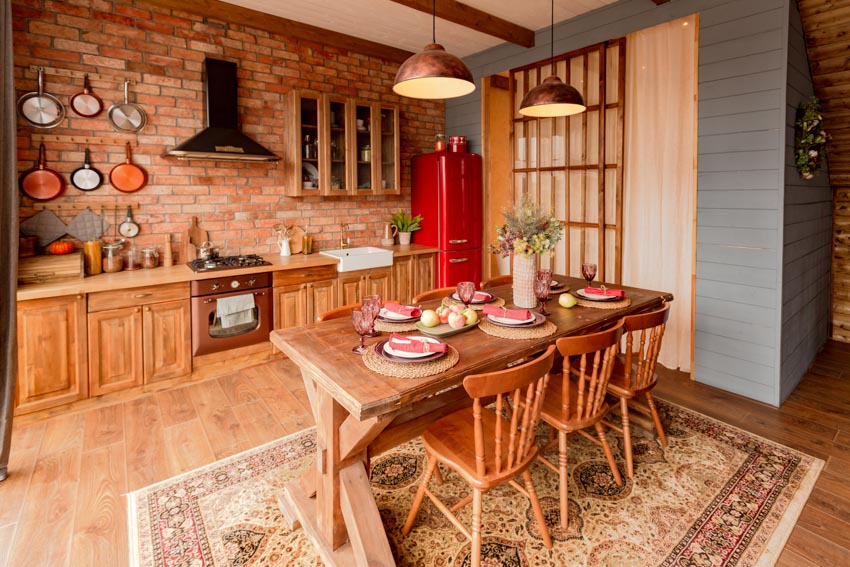 Rustic kitchen with brick backsplash, wood cabinets, countertop, table, chairs, and rug
