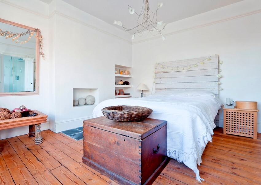 A rustic style bedroom interior with wooden floors, white walls and bed with chest box at foot part