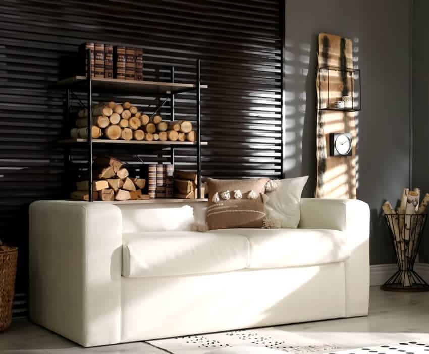 Shelving unit with stacked firewood, horizontal slat wall and comfortable sofa in stylish room interior