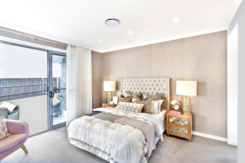 Spacious bedroom with headboard, nightstands, lamps, ceiling light, chair, bedding, and taupe walls