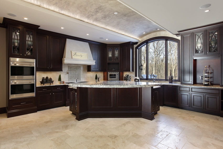 Spacious kitchen with wood cabinets, tile floors, island, range hood, travertine backsplash, ceiling lights, and windows