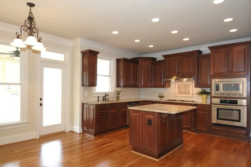 Spacious wooden kitchen with beige walls, chandelier, and brown granite countertops