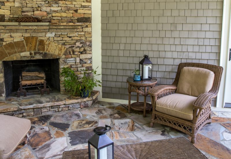 Stone patio floors of porch with an outdoor fireplace and rattan armchairs