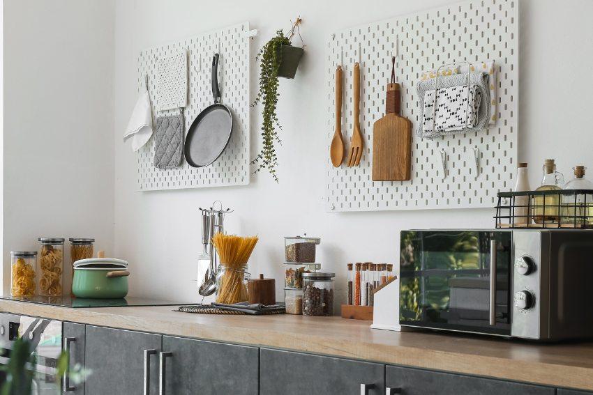 Stylish counters with utensils and pegboards on light wall in kitchen