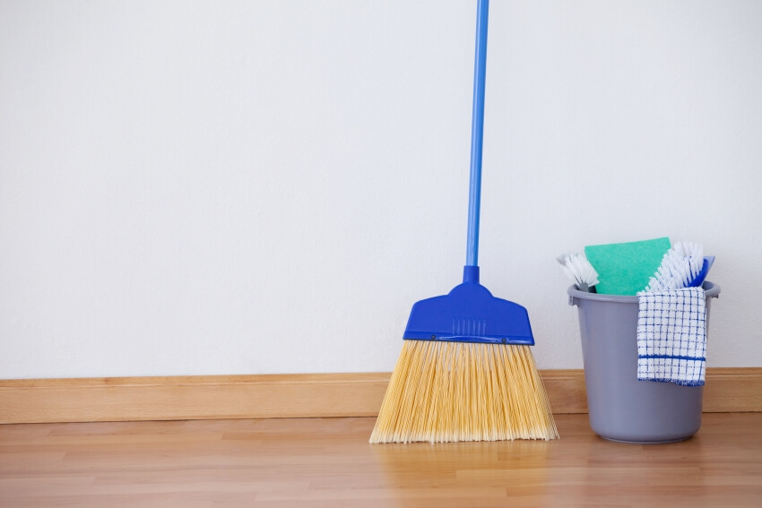 Various cleaning equipment including broom with flagged bristles on wooden floor against wall