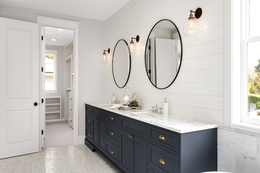 White bathroom with large vanity, dark blue cabinets, and circular mirrors on shiplap walls