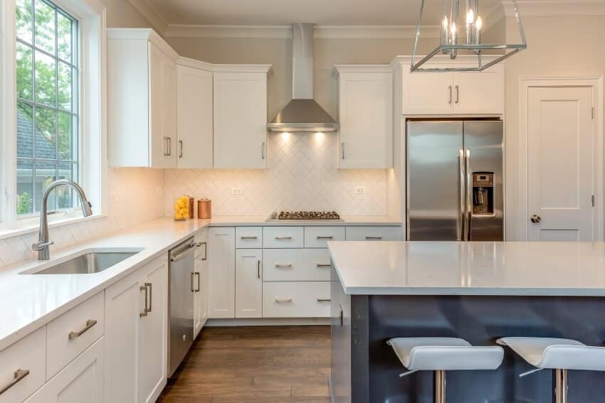 White kitchen with herringbone backsplash, chandelier over island, and silver hardware on cabinets