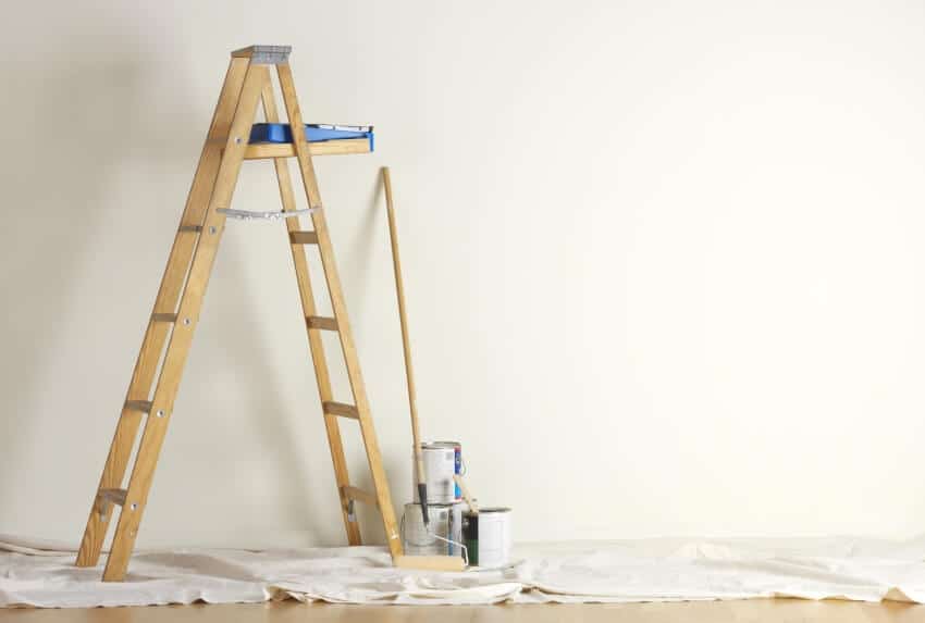 Wooden ladder, paint, and painting tools in an empty room