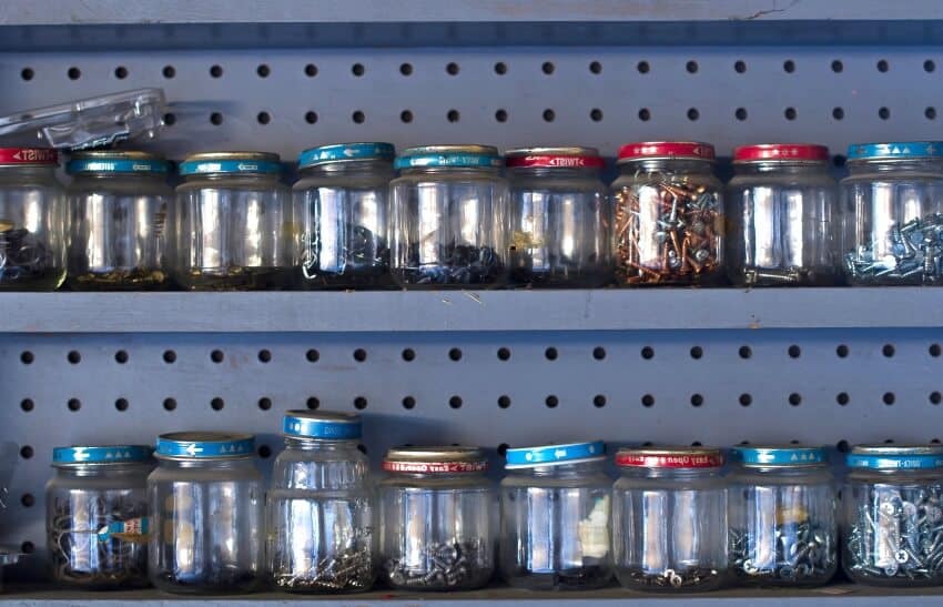 A wooden pegboard shelf row of glass jars holding screws and nails in the workshop
