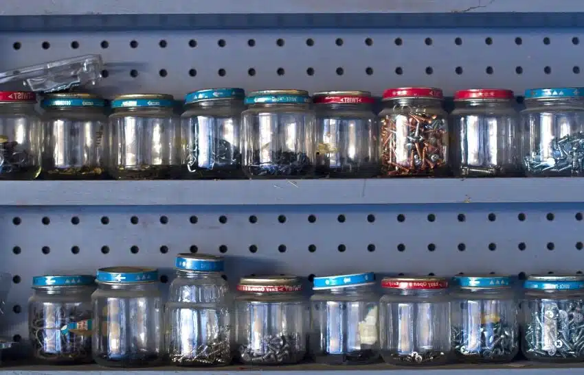 A wooden pegboard shelf row of glass jars holding screws and nails in the workshop