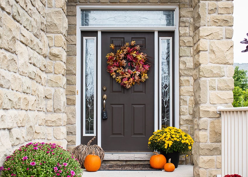 House entryway with dark brown front door with hanging wreath, glass sidelights stone brick wall