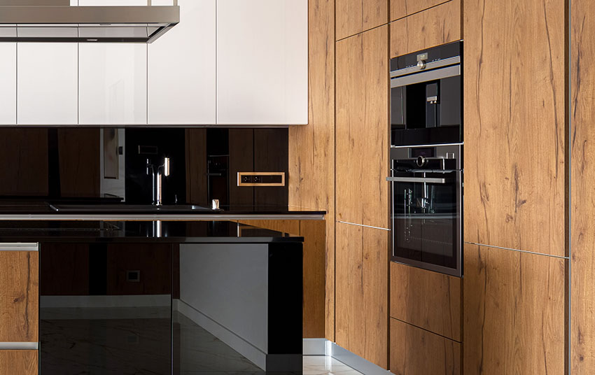 Modern kitchen with natural wood finish cabinets with ovens mounted black backsplash black granite countertop