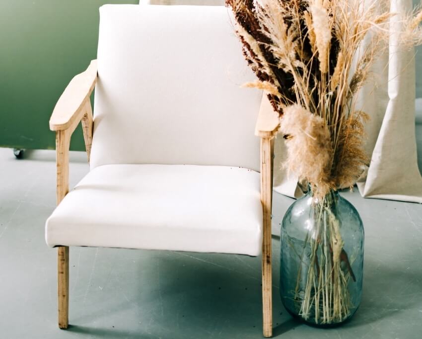 A stylish white chair next to an oversized large floor vase with dry branches as filler