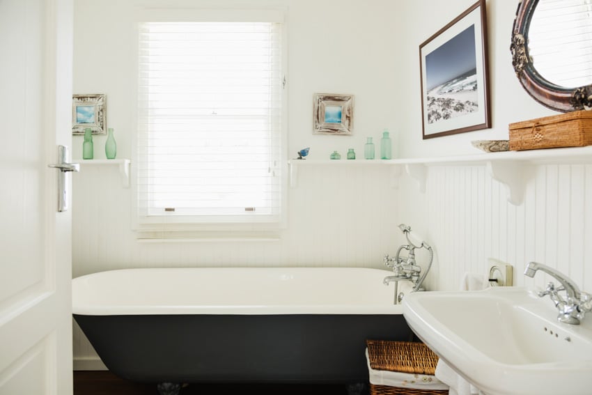 Bathroom with beadboard wall, tub, sink, mirror, shelves, and window