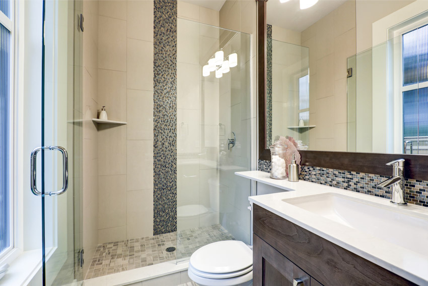Bathroom with glass door, mirror, countertop, sink, toilet, and waterfall tile shower