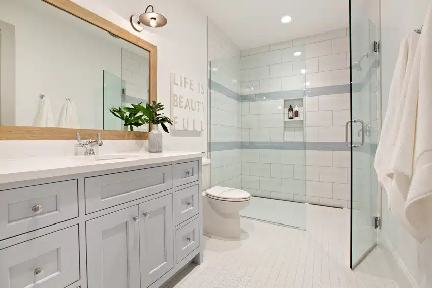 Bathroom with listello tile shower wall, glass door cabinets, toilet, countertop, and mirror
