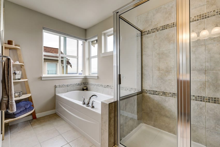 Bathroom with listello wall tile, glass enclosure, tub, windows, and tile flooring