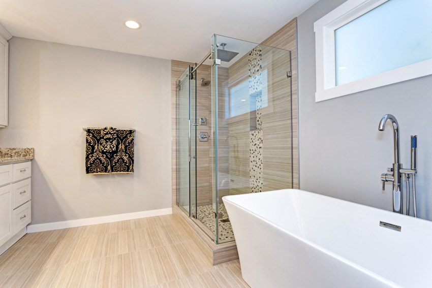 Bathroom with pebble tile feature wall shower, tub, glass enclosure, window, ceiling light, and wood flooring