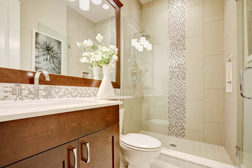 Bathroom with waterfall tile shower, glass door, countertop, vanity, mirror, toilet, and cabinet