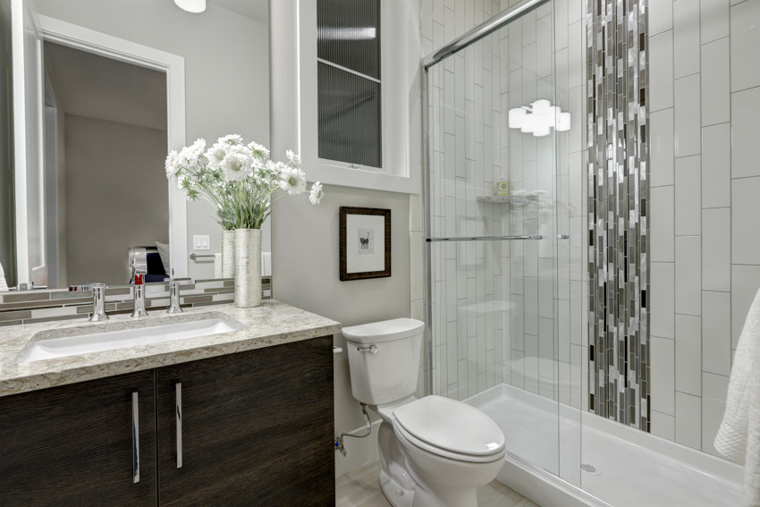 Bathroom with waterfall inlay tile shower, toilet, glass door, countertop, mirror, cabinet, and sink
