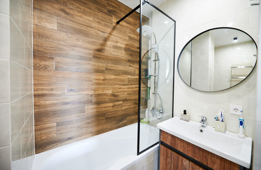 Bathroom with wood shower wall, mirror, sink, and half glass shower door for bathtub