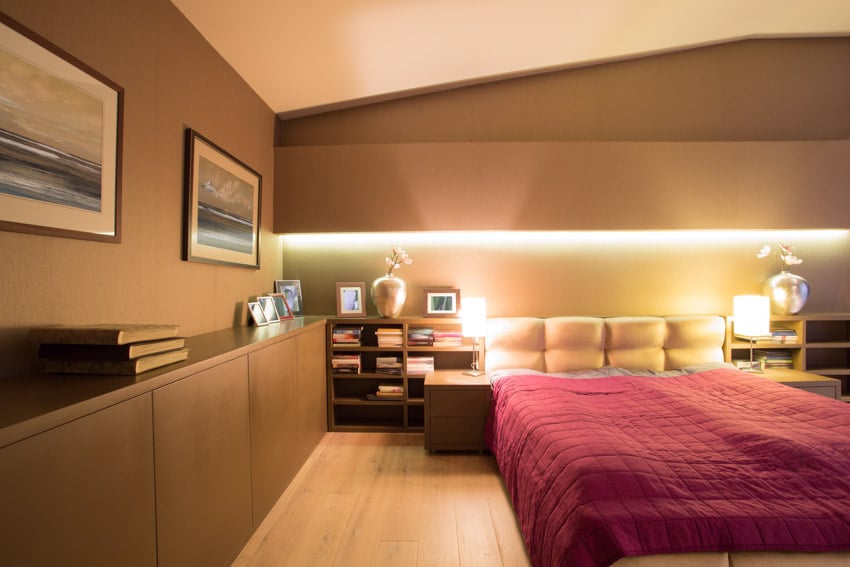 Bedroom with red comforter, pillows, wood cabinets and brown walls